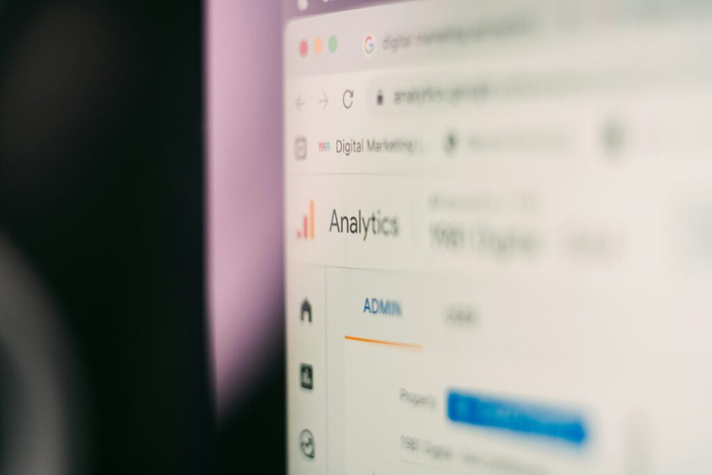 Close-up of a laptop and notebook on a desk with a blurred digital marketing dashboard on a screen in the background